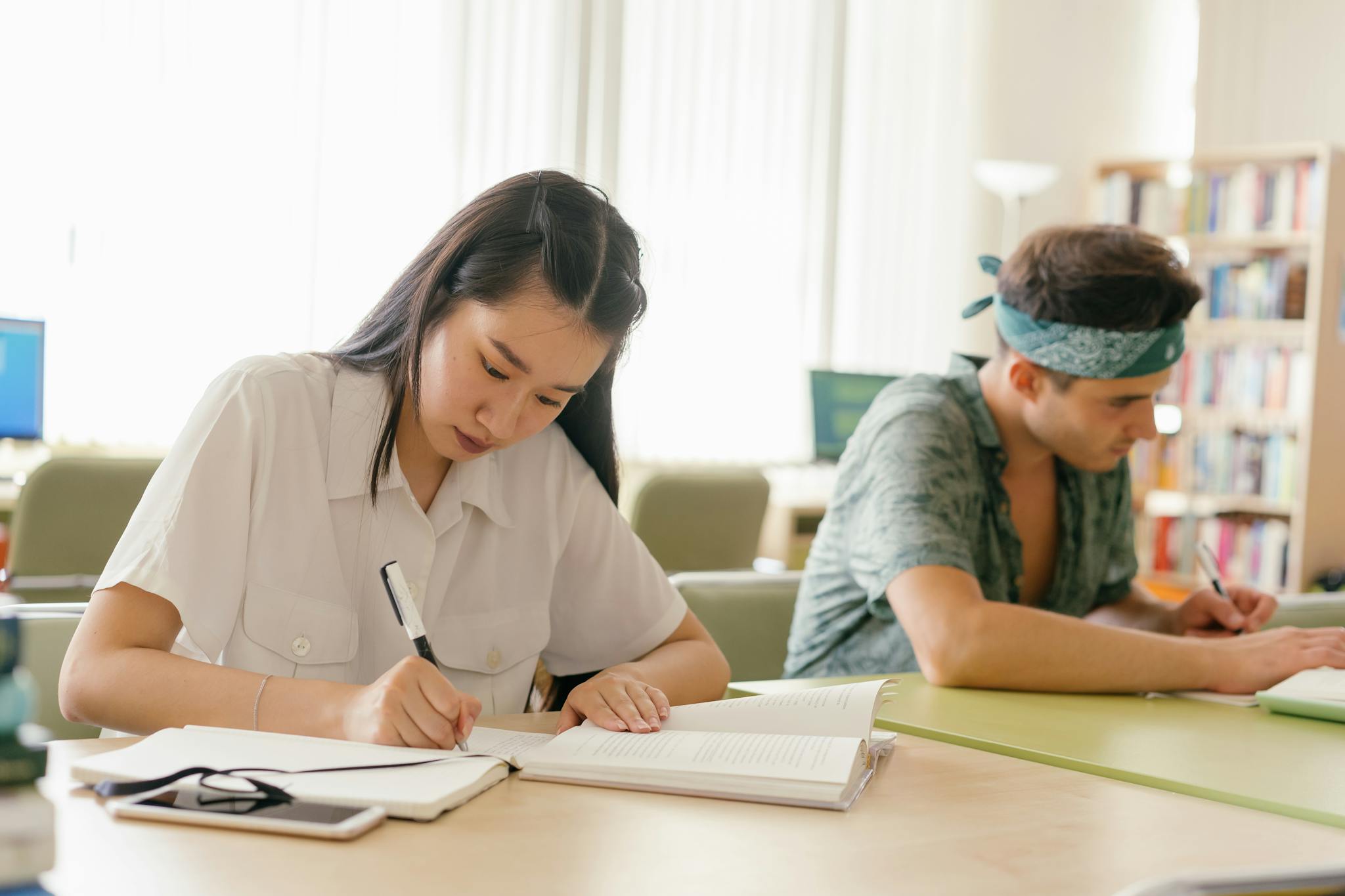 Asian woman and Caucasian man diligently studying in a bright library environment.