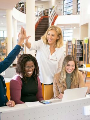 Cheerful diverse group of students collaborating in a library, celebrating with a high five.