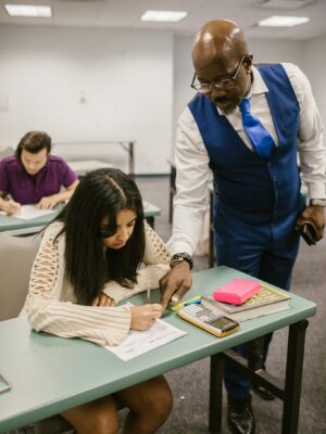 Educator assisting student during an exam in a classroom setting, emphasizing support in education.