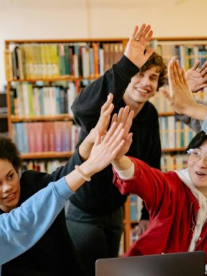 Group of happy students high-fiving in a library setting, celebrating success.