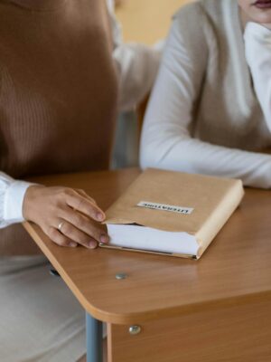 Two students sitting together at a classroom desk with a book titled 'Literature' and stationery items.